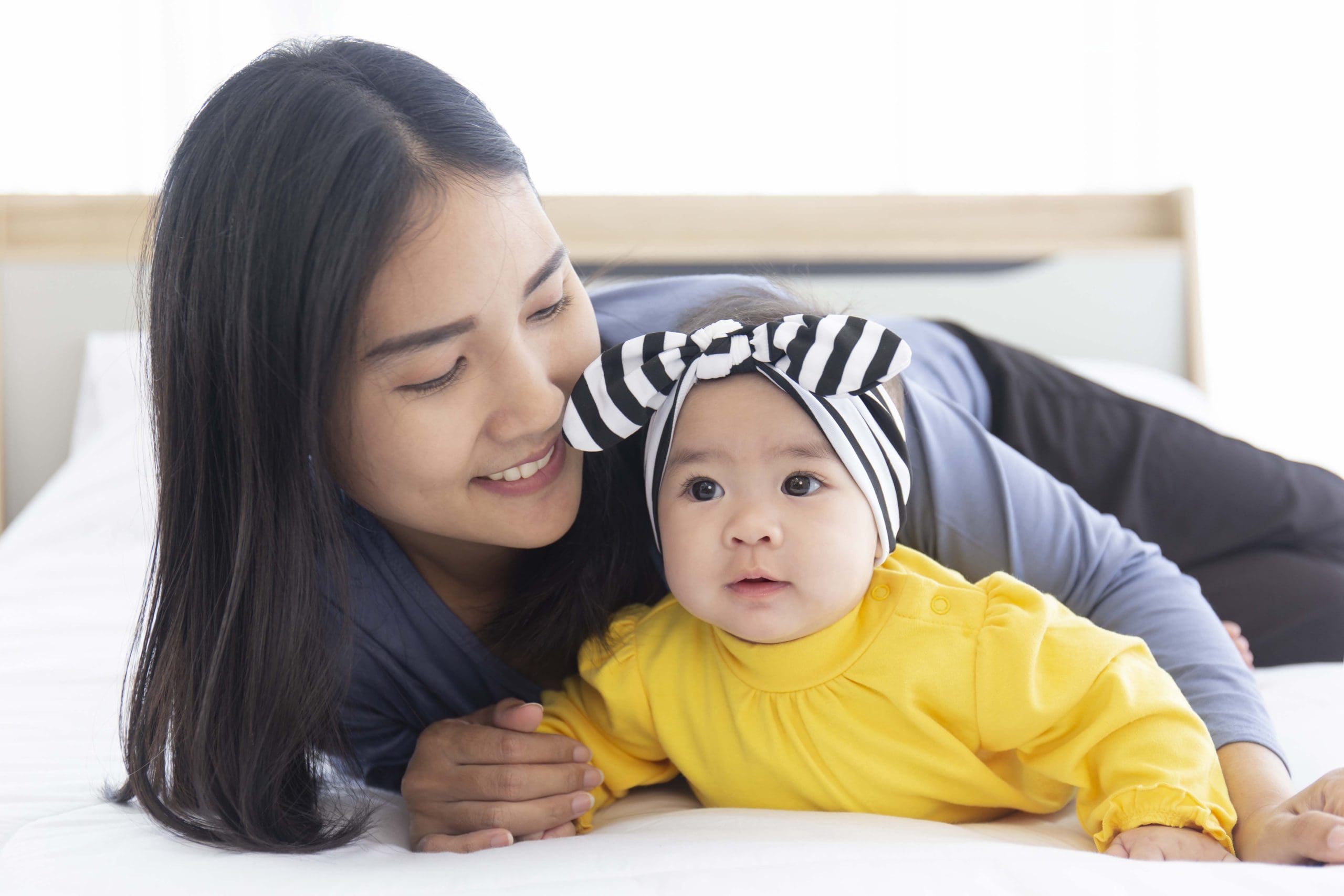 An Asian mom plays with her baby in bed with love and care