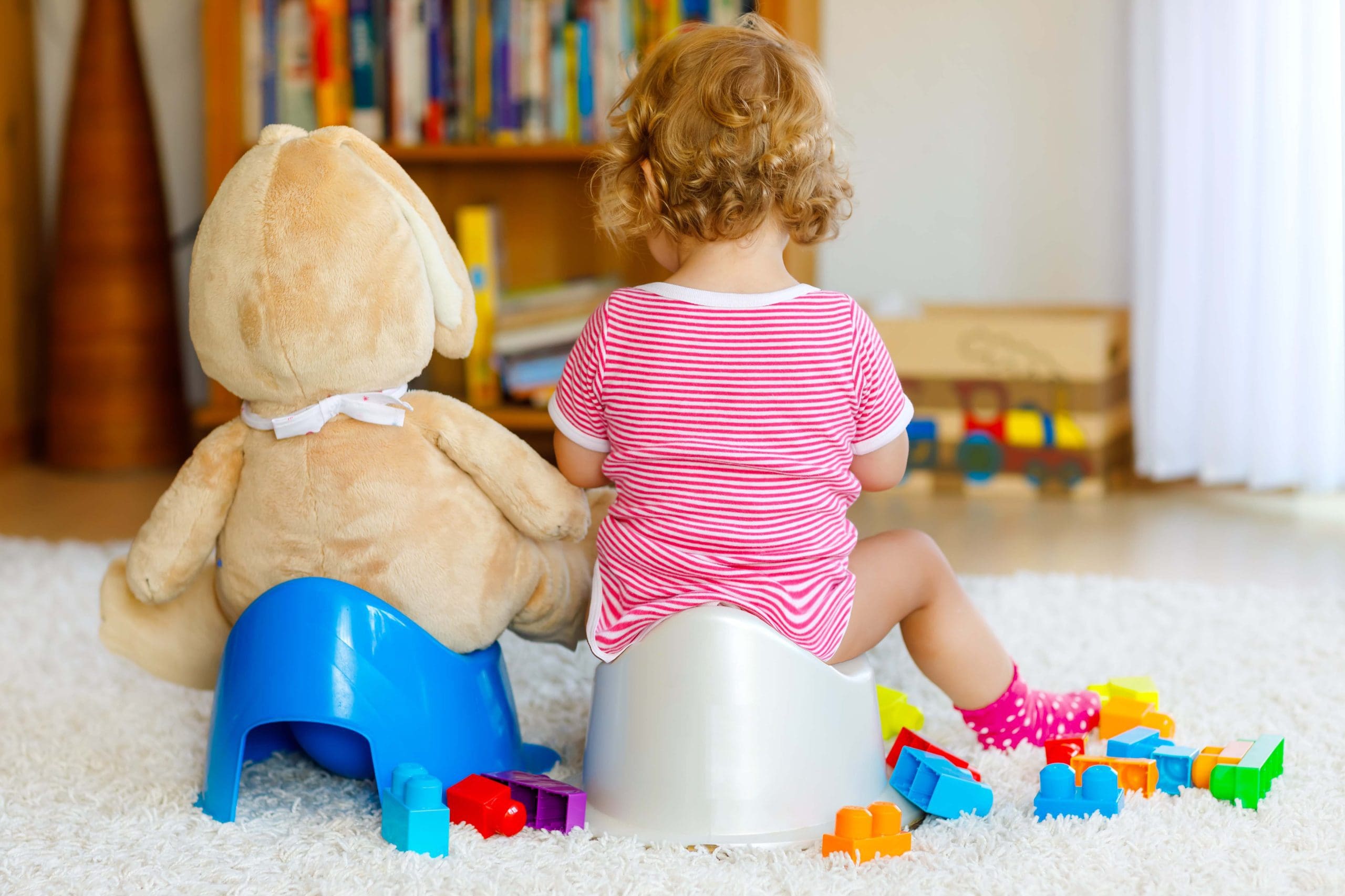 Closeup of cute little 12 months old toddler baby girl child sitting on potty. Kid playing with big plush soft toy. Toilet training concept